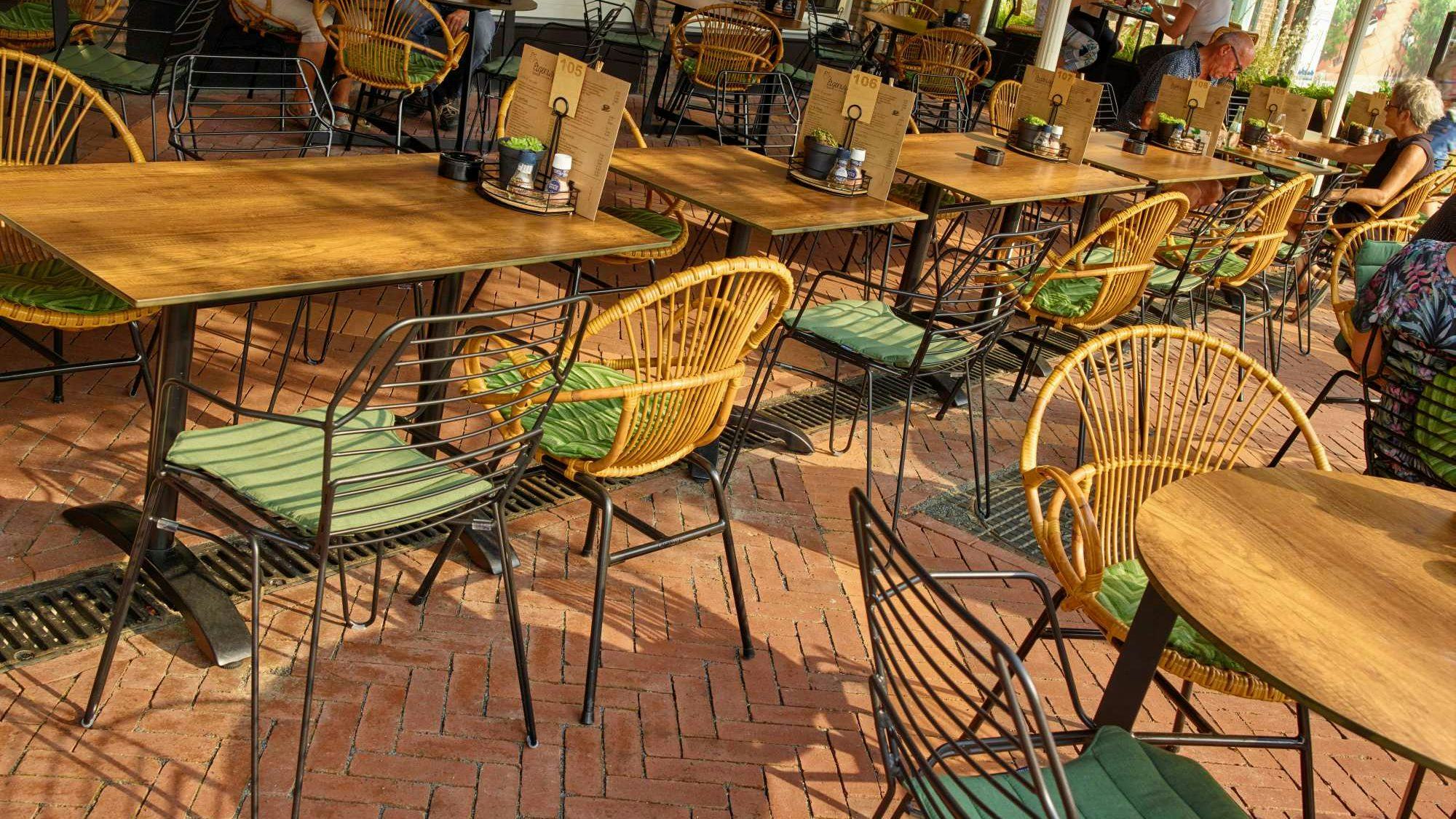 Het terras van Eigenwijs eten & drinken in Oostburg is een mix & match van modern draadstaal meubilair en weerbestendige rotanlook stoelen, geïnspireerd op de sixties. De groene zitkussens maken het warme terras af. Meubilair: Satelliet. 