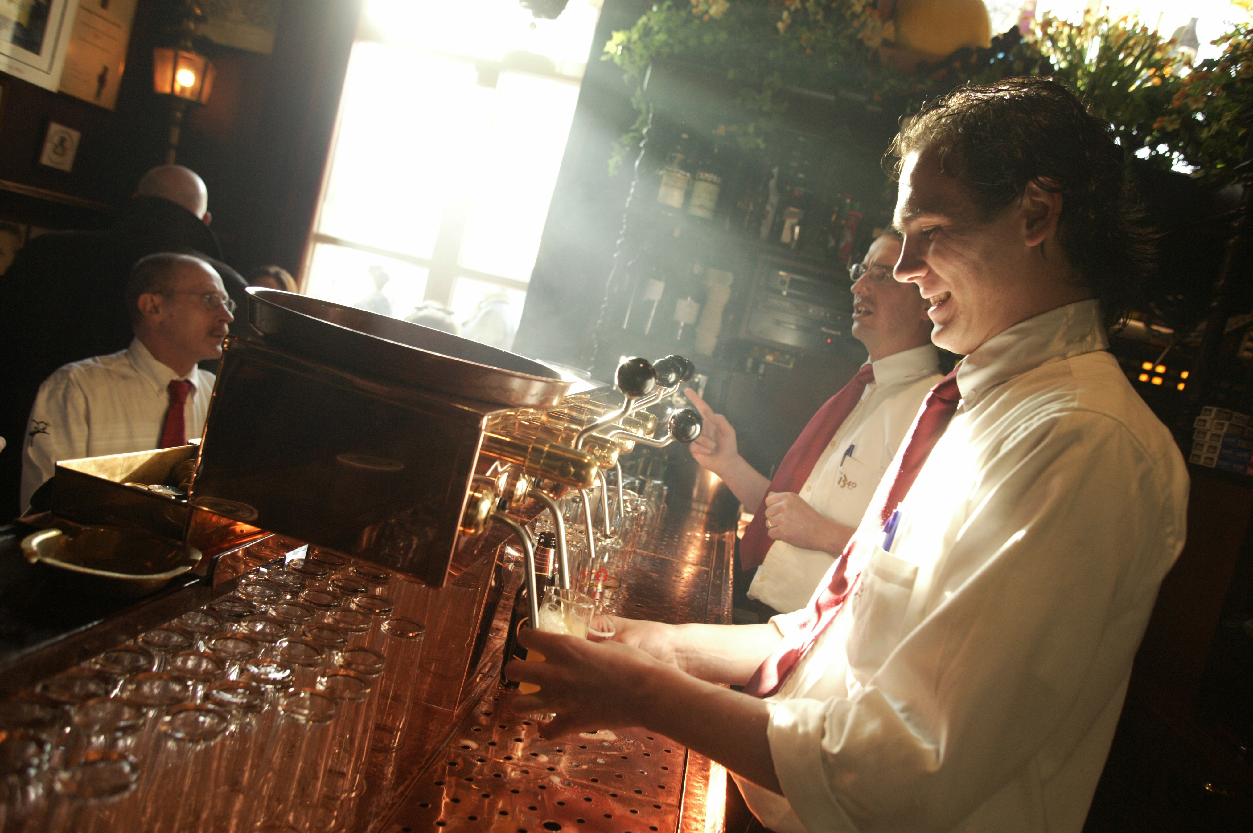 Een medewerker van café In den Ouden Vogelstruys in Maastricht tapt glazen bier uit de tapkranen achter de bar.