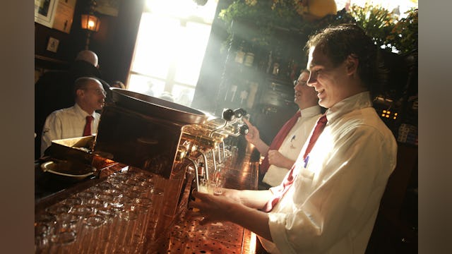 Een medewerker van café In den Ouden Vogelstruys in Maastricht tapt glazen bier uit de tapkranen achter de bar.