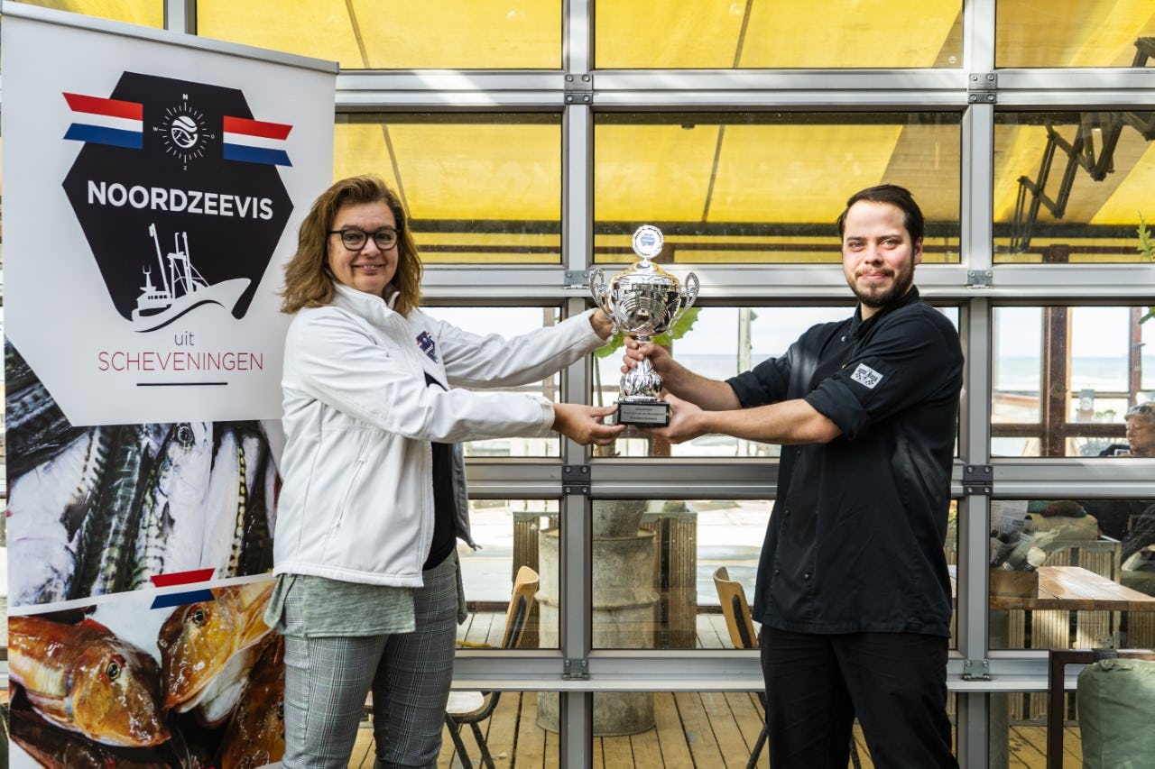 Suzanne van der Pijll, bestuurslid Stichting Noordzeevis uit Scheveningen overhandigt de trofee aan Tobias Smallenbroek, Chef-kok Strandtent Solbeach Scheveningen
