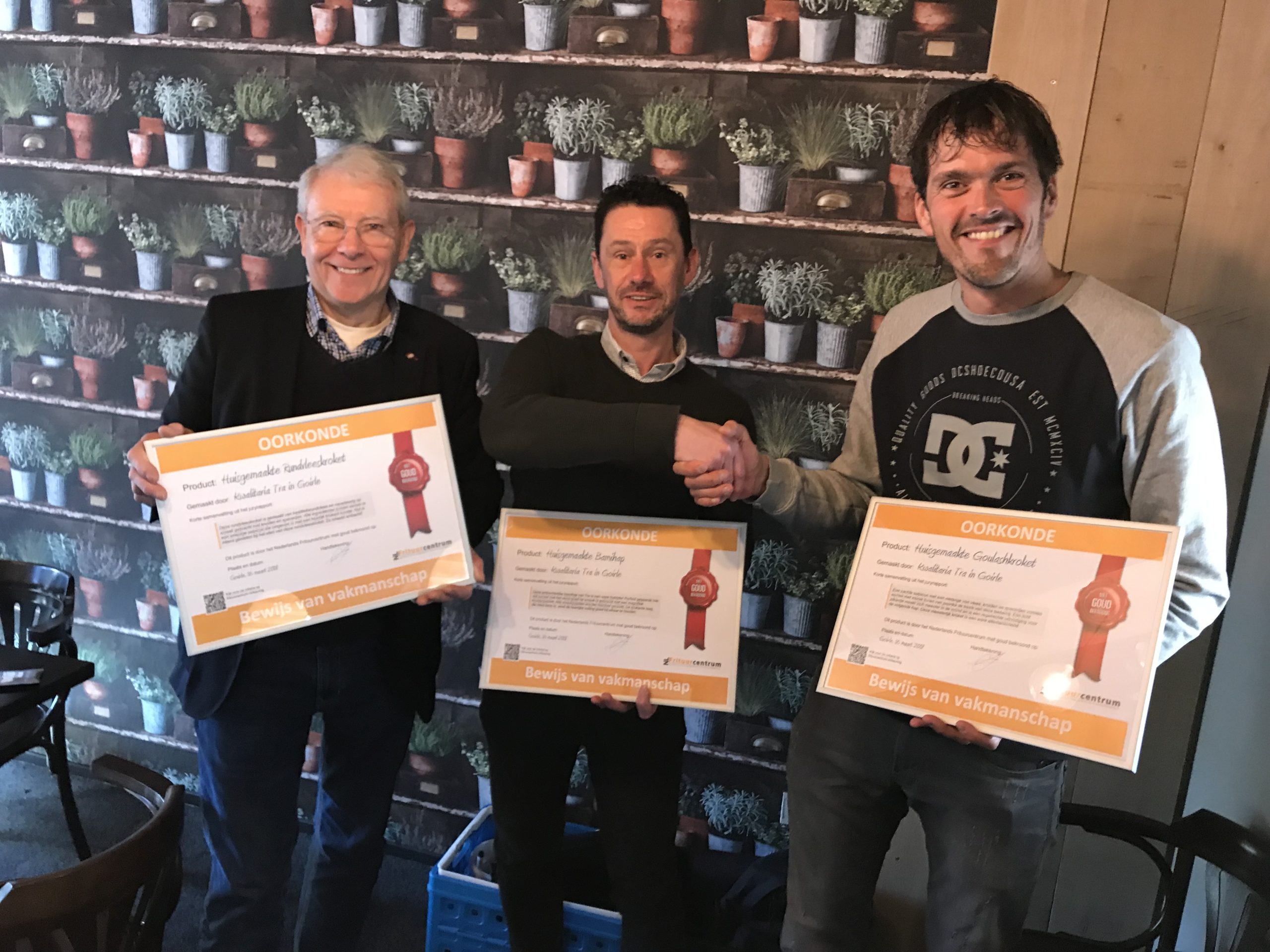 ProFri-bestuurder Jorgen Ruhl (rechts op de foto) reikt de oorkondes uit voor drie huisgemaakte snacks van Kwalitaria Tra. Links op de foto  Berry Tra en zijn zoon Ad in het midden namen het bewijs van vakmanschap in ontvangst. 