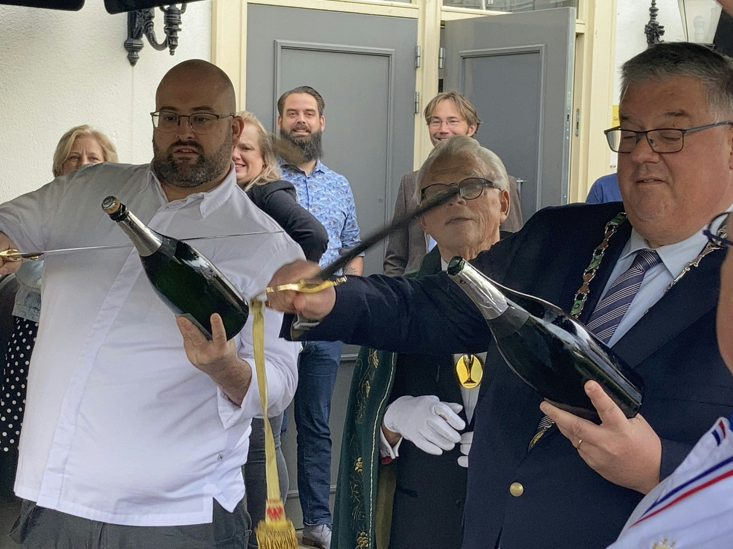 Manuel Jansen (l) en burgemeester Bruls sabreren een fles champagne als officiële inauguratie-handeling.