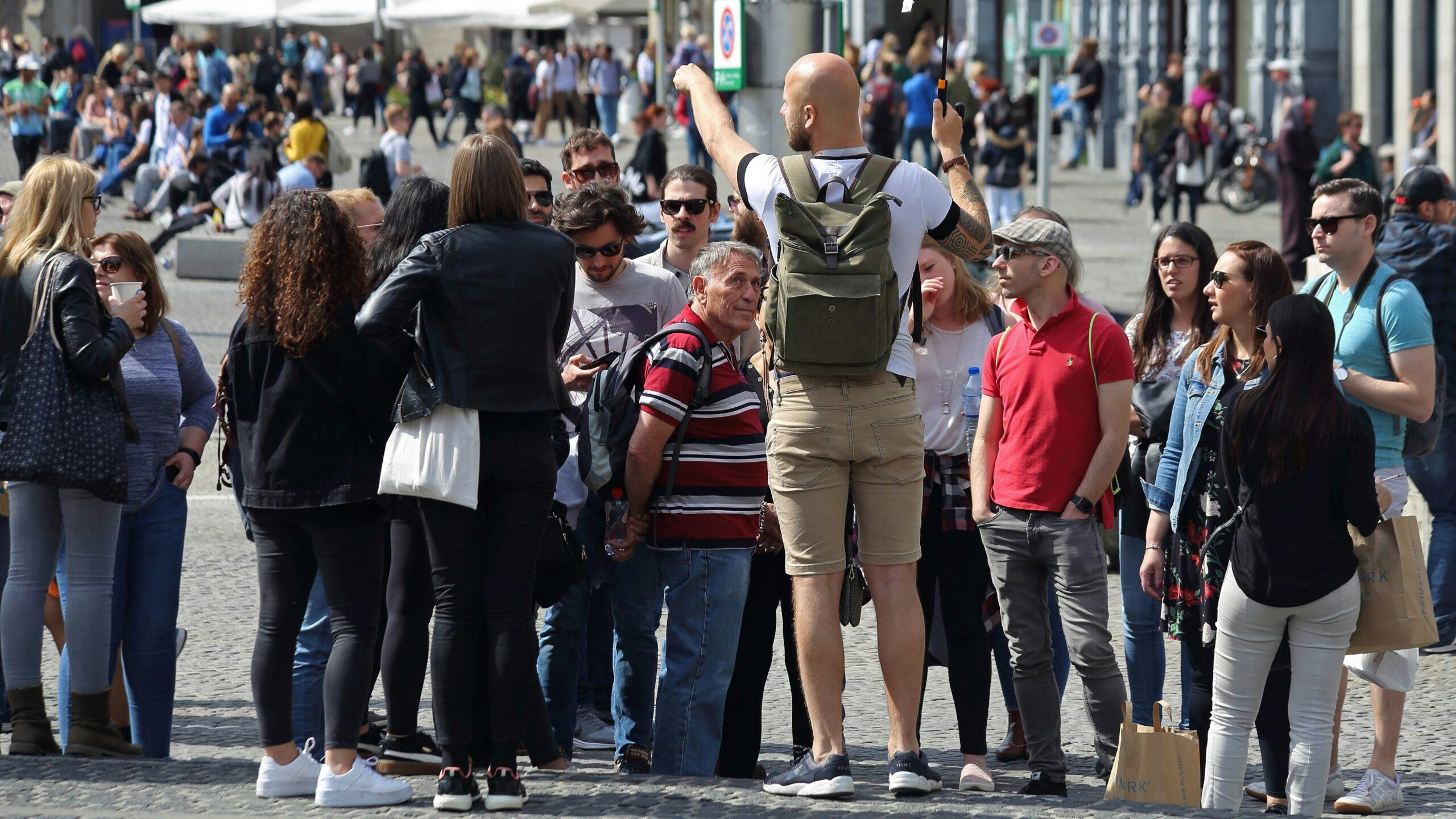 Tour guide with an umbrella and a group of tourists on Dam square in Amsterdam, The Netherlands on May 23, 2019